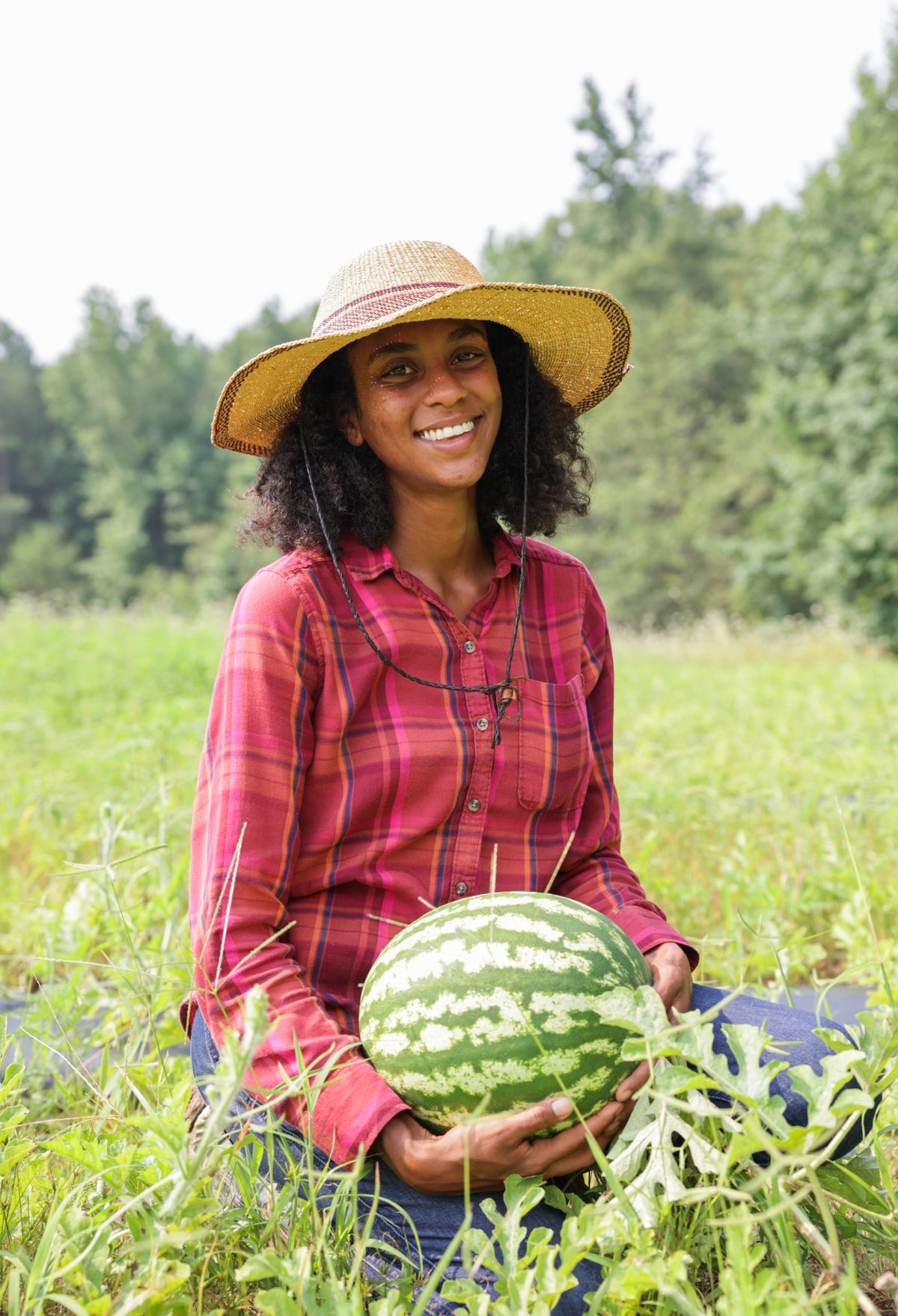A smiling woman holding a watermelon in a field.