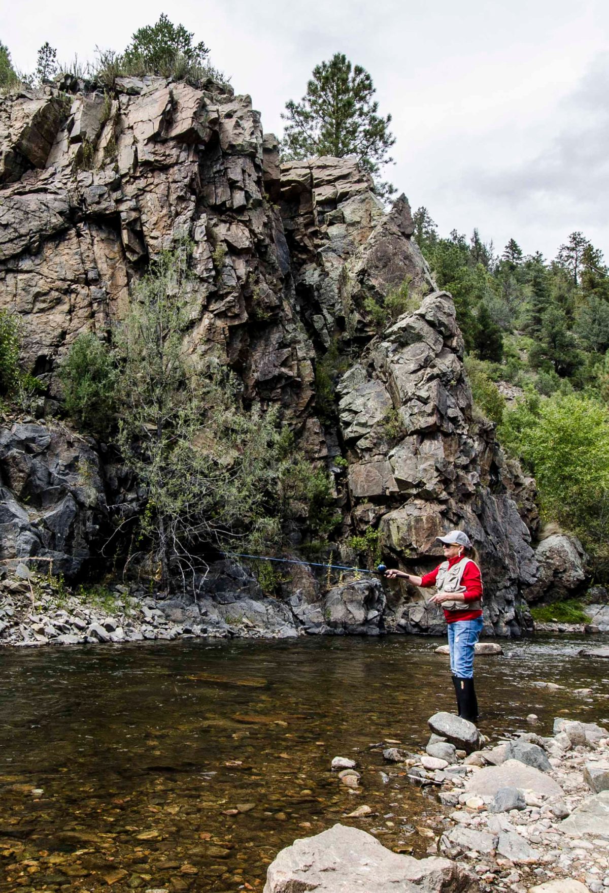 A person fly-fishing near a cliffside lake.