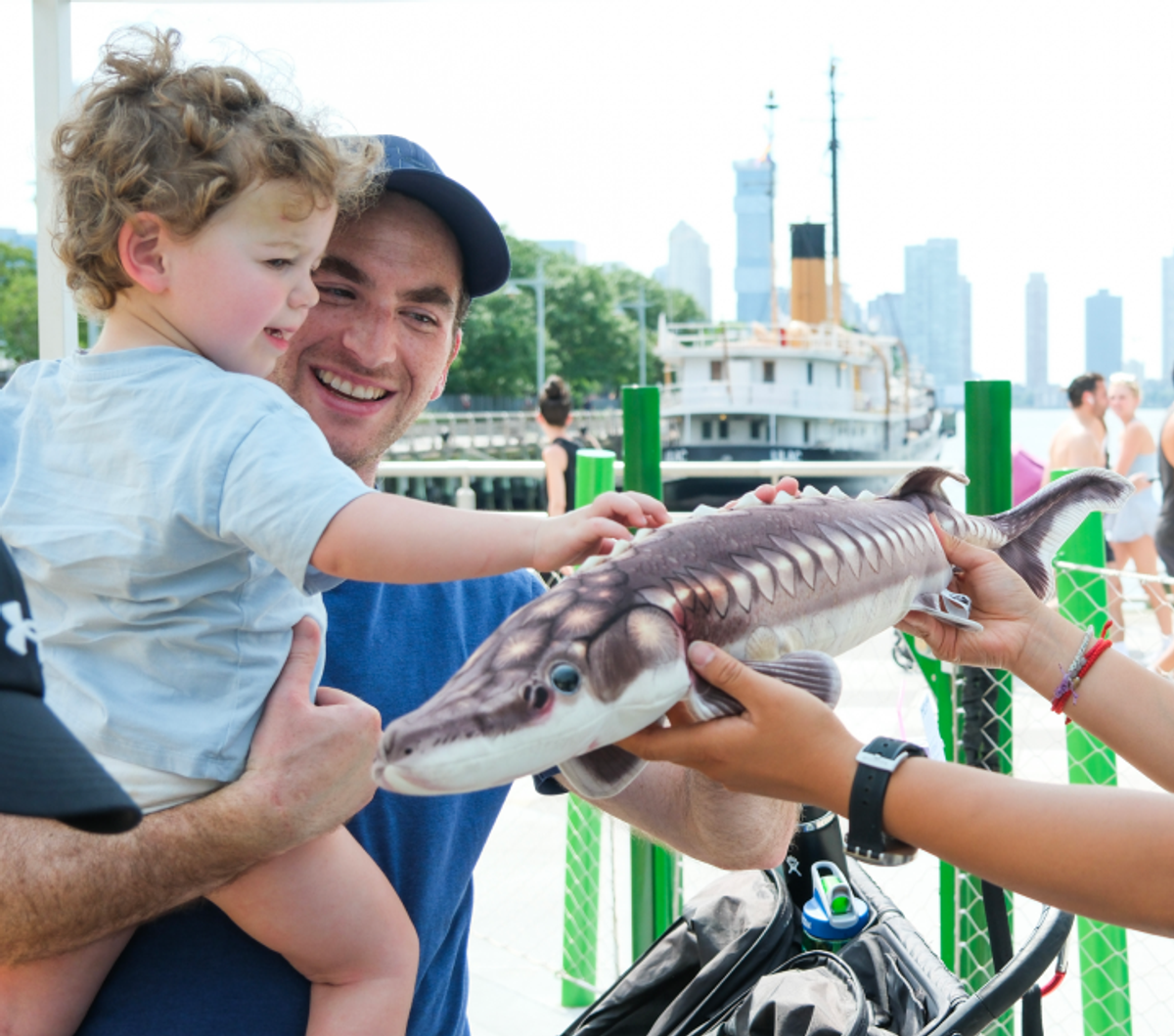 Image of a man holding a child, touching a fish being held out towards him
