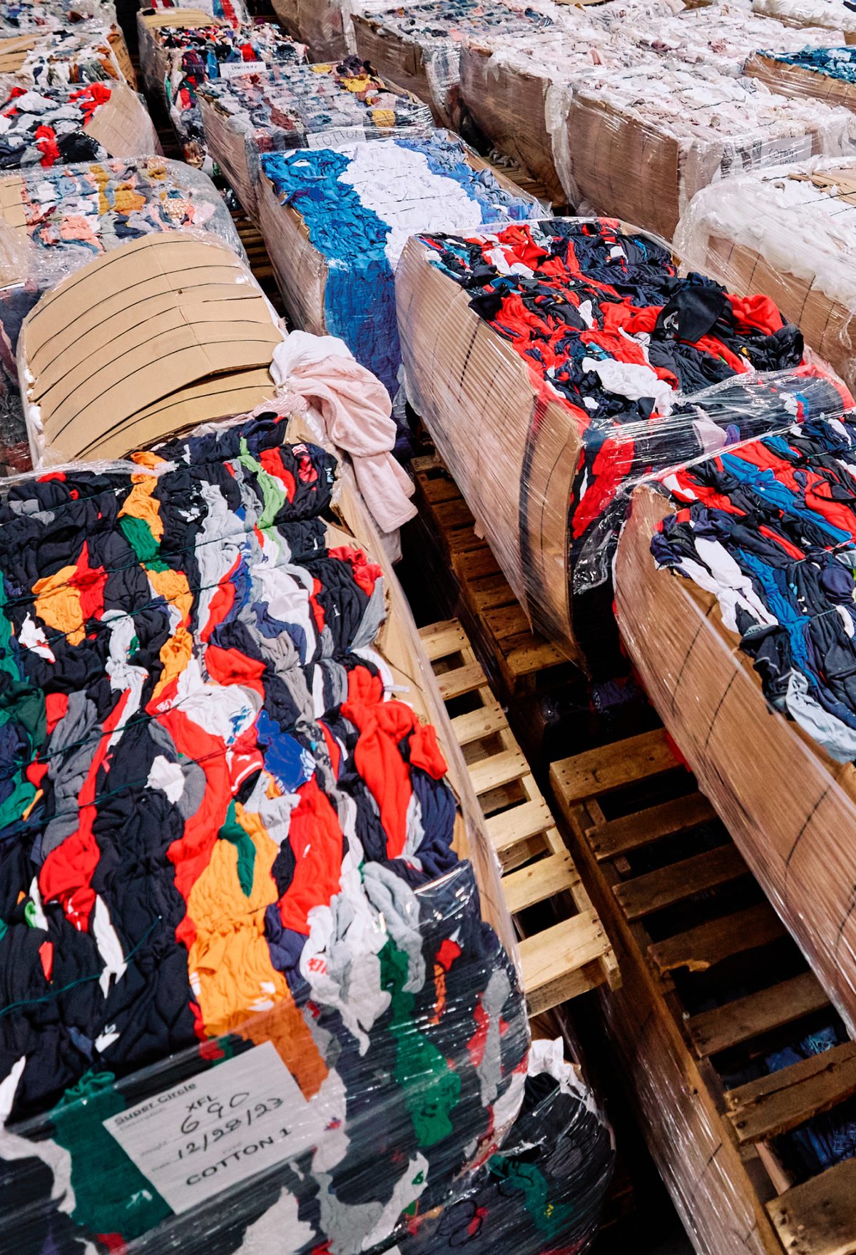 Many large bins of old shirts on wooden pallets.